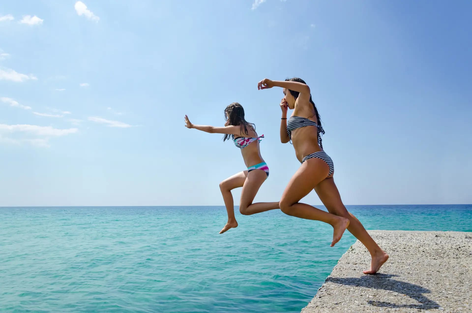 Two swimmers leaping into the turquoise water off a Zanzibar pier